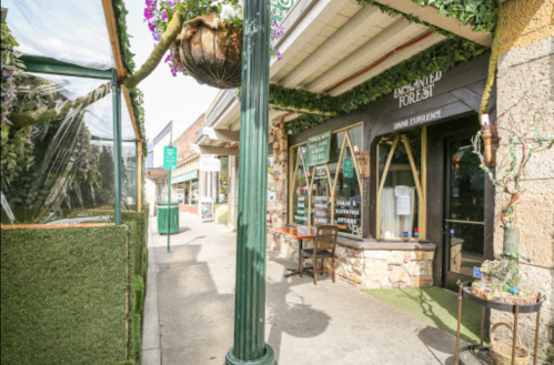 A charming street view featuring a café with greenery and a cozy outdoor seating area.