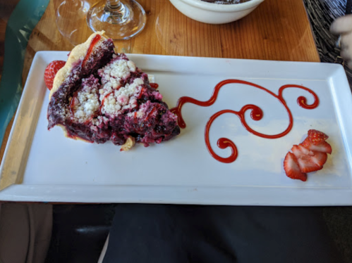 A slice of berry pie on a white plate, decorated with a swirl of sauce and fresh strawberry slices.