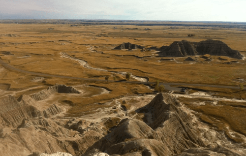 A panoramic view of rugged, dry terrain with rolling hills and sparse vegetation under a clear sky.