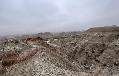 A vast, rugged landscape of eroded hills and valleys under a cloudy sky, showcasing earthy tones and textures.
