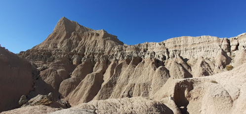 A rugged, arid landscape with steep, layered rock formations under a clear blue sky.