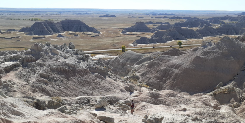 A vast landscape of rugged, eroded hills and valleys under a clear blue sky, showcasing natural geological formations.