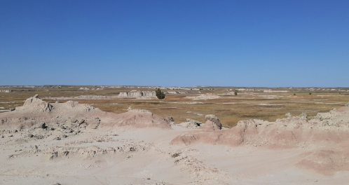 A vast, arid landscape with layered rock formations under a clear blue sky.