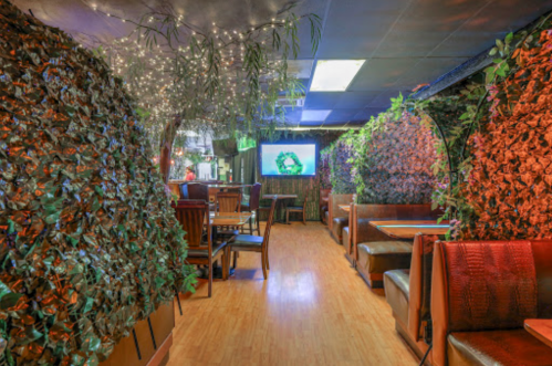 A cozy restaurant interior with green foliage walls, soft lighting, and wooden booths along a narrow corridor.