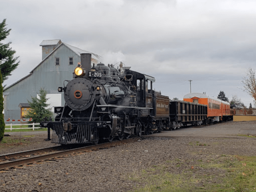 A vintage steam locomotive with a black engine and orange passenger car on a track, set against a cloudy sky.