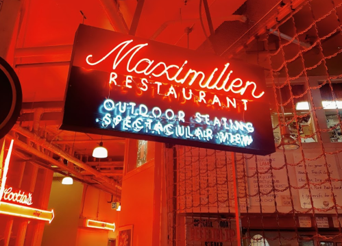 Neon sign for Maximilien Restaurant, highlighting outdoor seating and a spectacular view, illuminated in red light.
