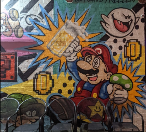 Colorful mural featuring a cartoon character resembling a plumber, holding a drink and a mushroom, with playful background elements.