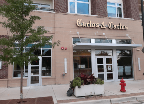 Exterior of a restaurant named "Carlos & Carlos," featuring large windows and a decorative planter.