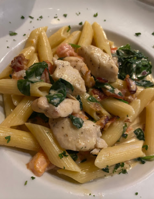A plate of penne pasta with chicken, spinach, and bacon in a creamy sauce, garnished with parsley.