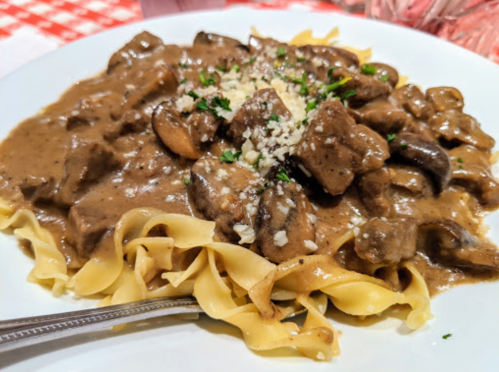 A plate of egg noodles topped with beef stroganoff, mushrooms, and a sprinkle of parsley and cheese.