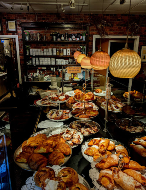 A display of various pastries and baked goods in a cozy bakery, with warm lighting and a rustic brick backdrop.