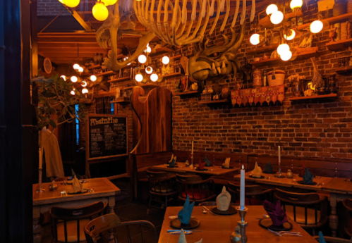 Cozy restaurant interior with wooden tables, unique decor, and warm lighting, featuring a large skeleton hanging from the ceiling.