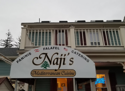 Sign for Naji's Mediterranean Cuisine, featuring paninis, falafel, and catering services, on a building exterior.