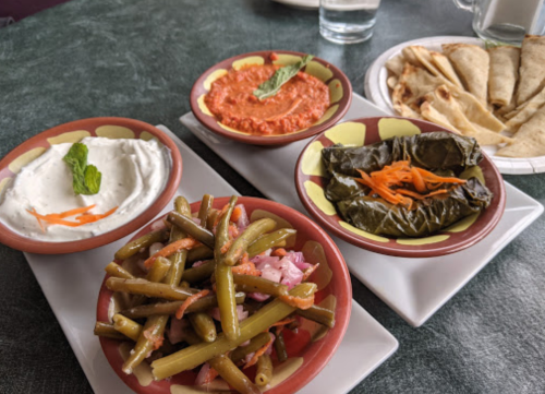 A table with four small bowls of various dips and dishes, including green beans, yogurt, red dip, and stuffed grape leaves.