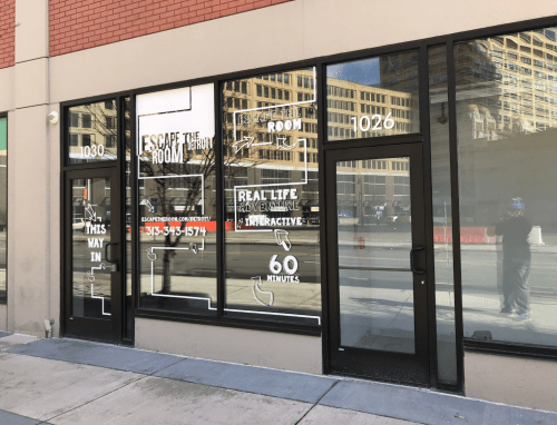 Exterior of an escape room venue with large windows displaying the name and details about the interactive experience.