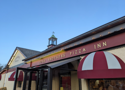 Exterior of Four Brothers Pizza Inn, featuring a red and white striped awning and a decorative cupola.