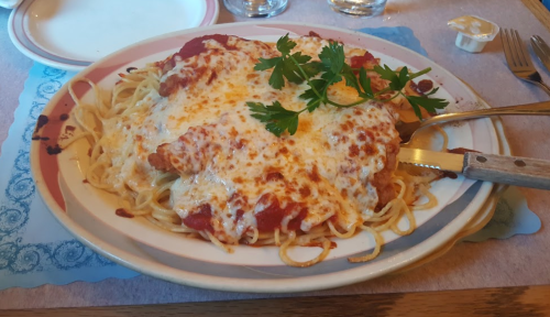 A plate of spaghetti topped with marinara sauce, melted cheese, and parsley, served with a fork and knife.