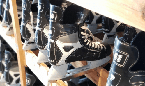 A row of black and white ice skates neatly arranged on wooden shelves.