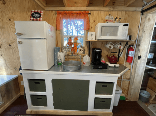 A cozy kitchen area with a fridge, microwave, coffee maker, and decorative items on a wooden countertop.