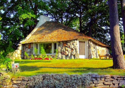A charming stone cottage with a thatched roof, surrounded by lush greenery and colorful flowers.