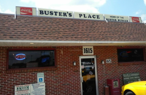 Exterior of Buster's Place, a restaurant featuring a sign for the Buster Burger, with a brick facade and open sign.