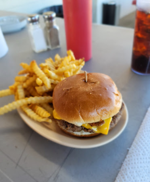 A cheeseburger with a slice of cheese and a side of crinkle-cut fries on a plate, with condiments in the background.