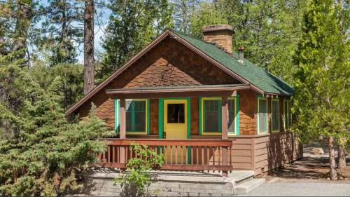 A charming wooden cabin with a green roof, yellow door, and surrounded by trees in a serene outdoor setting.