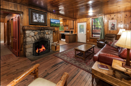 Cozy wooden living room with a stone fireplace, leather sofa, and rustic decor, featuring warm lighting and a welcoming atmosphere.