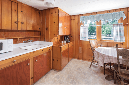 Cozy kitchen with wooden cabinets, a sink, microwave, coffee maker, and a small dining table by a window.