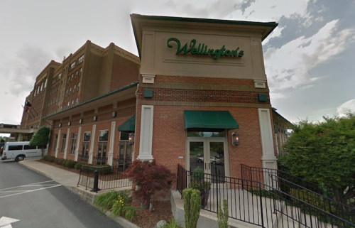 Exterior view of Wellington's restaurant, featuring a brick facade and green signage, with a parking area in front.