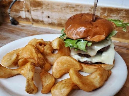 A juicy burger with lettuce and melted cheese, served with crispy potato wedges on a white plate.