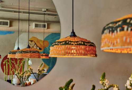 Three woven pendant lamps hang against a textured wall with colorful artwork, creating a warm, inviting atmosphere.