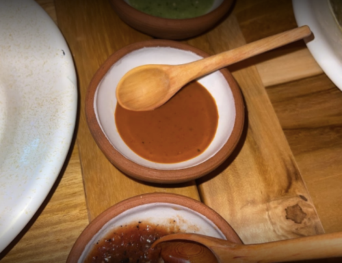 Three small bowls of sauces on a wooden platter, with a wooden spoon in the brown sauce.