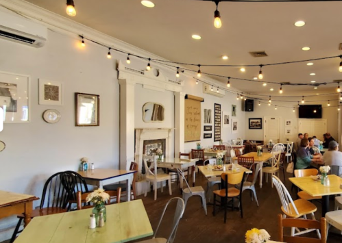 Cozy restaurant interior with wooden tables, string lights, and a mix of chairs, creating a warm atmosphere.
