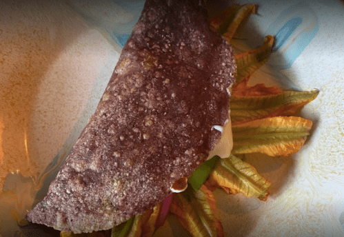 A close-up of a purple tortilla filled with colorful vegetables, resting on a decorative plate.