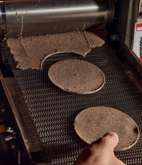 A hand places round patties of dough onto a conveyor belt machine for processing.