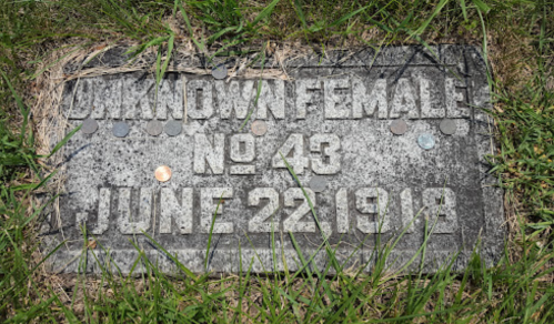 Gravestone marked "Unknown Female No. 43, June 22, 1918," surrounded by grass and coins.