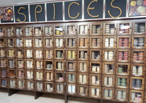 A wooden spice rack filled with various jars and containers, labeled and organized, under a sign that reads "SPICES."