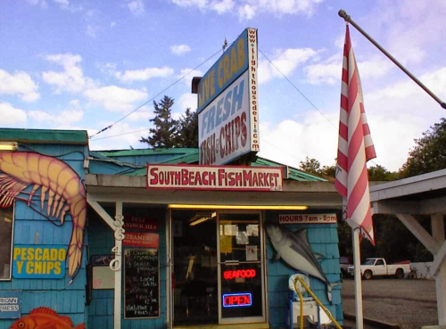 Exterior of South Beach Fish Market with a colorful sign, open hours displayed, and a flag waving in the breeze.