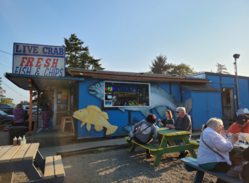 A seafood restaurant with a colorful mural, outdoor seating, and customers enjoying fish and chips on a sunny day.