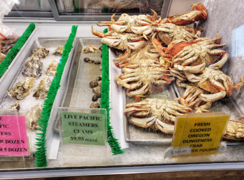 A seafood display featuring live crabs, clams, and fresh cooked Dungeness crab with price signs.