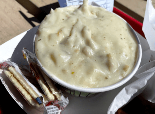 A bowl of creamy mashed potatoes with herbs, accompanied by two packets of crackers on a tray.