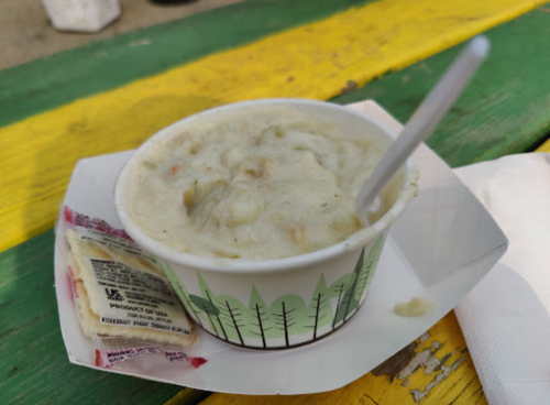 A cup of creamy soup with vegetables, accompanied by a packet of crackers, on a colorful wooden table.