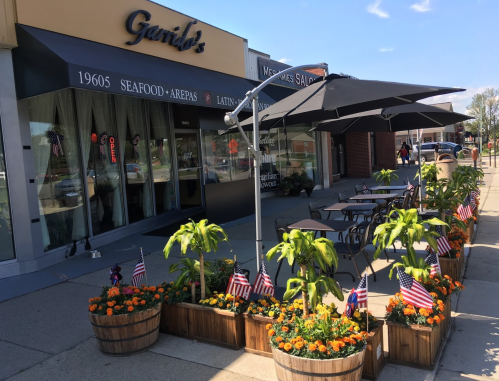 Outdoor seating area with planters and flags in front of a seafood restaurant, featuring umbrellas and vibrant flowers.