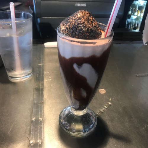 A tall glass filled with layers of chocolate syrup, whipped cream, and a scoop of ice cream, topped with a straw.