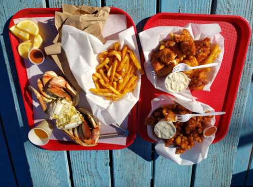 Two red trays with seafood, fries, and dipping sauces on a blue wooden surface.