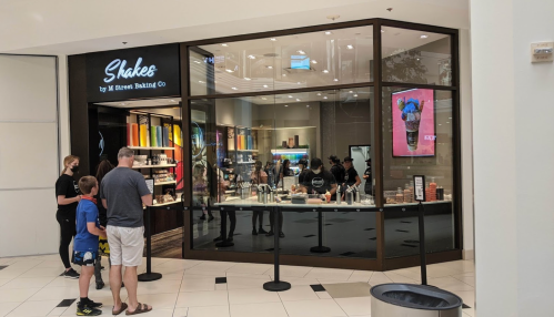 A family stands outside a shake shop in a mall, looking at the menu displayed in the window.