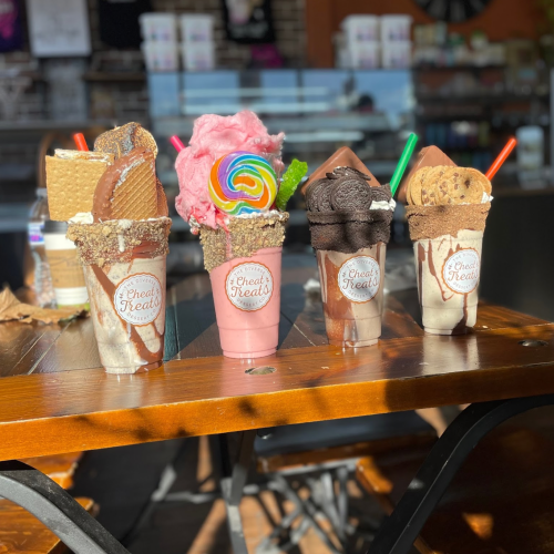 A variety of colorful milkshakes topped with sweets, served in decorative cups on a wooden table.