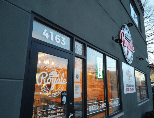 Exterior of "Royale with Cheese" restaurant, featuring large windows and a sign indicating it's open.
