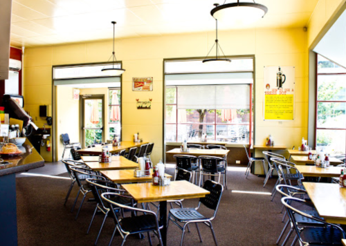 Bright, spacious diner interior with wooden tables, metal chairs, and large windows letting in natural light.